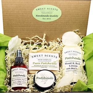 May include: A gift box filled with a variety of bath and body products in a patchouli scent. The box contains a bar of soap, a bottle of lotion, a bottle of spray, and a jar of body butter. The products are all labeled with the brand name "Sweet Scents" and the scent "Patchouli".