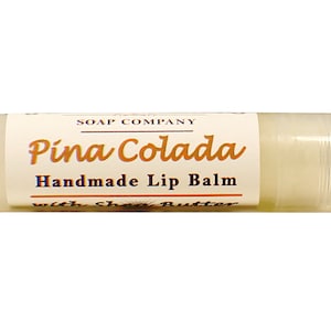 K&ouml;nnte beinhalten: Eine wei&szlig;e Tube mit Pina Colada Lippenbalsam mit einem wei&szlig;en Etikett, auf dem "SOAP COMPANY Pina Colada Handgemachter Lippenbalsam mit Sheabutter" steht.