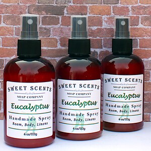Pu&ograve; includere: Tre bottiglie di vetro marrone con spruzzini neri ed etichette bianche. Le etichette riportano "Sweet Scents Soap Company Eucalyptus Handmade Spray Room, Body, Linens 4 oz/113g".