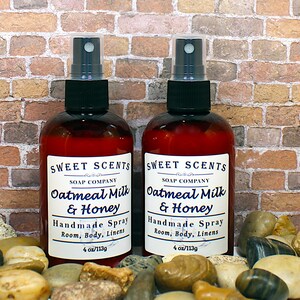 May include: Two 4-ounce bottles of oatmeal milk and honey scented room spray. The bottles are brown glass with black spray tops and white labels that read "Sweet Scents Soap Company Oatmeal Milk & Honey Handmade Spray Room, Body, Linens 4 oz/113g".