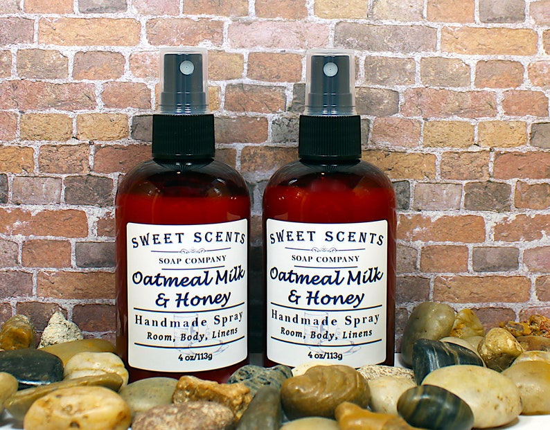 May include: Two 4-ounce bottles of oatmeal milk and honey scented room spray. The bottles are brown glass with black spray tops and white labels that read "Sweet Scents Soap Company Oatmeal Milk & Honey Handmade Spray Room, Body, Linens 4 oz/113g".