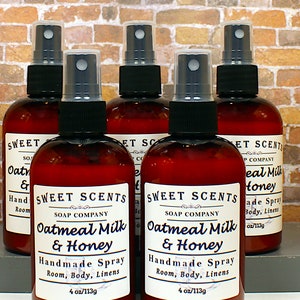 May include: Six brown glass bottles with spray tops filled with a clear liquid. The bottles have white labels with black text that reads "Sweet Scents Soap Company Oatmeal Milk & Honey Handmade Spray Room, Body, Linens 4 oz/113g".