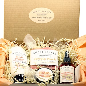 May include: A gift box filled with peach-scented bath and body products from Sweet Scents Soap Company. The box contains a bottle of hand and body lotion, a bar of soap, a jar of body butter, and a bottle of room spray. All products are labeled with the scent "Peach Passion" or "Georgia Peach".