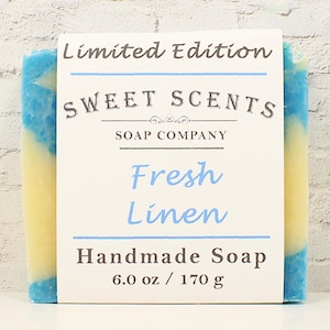 May include: A handmade soap bar with blue and yellow hues, labeled "Fresh Linen" by Sweet Scents Soap Company. The label reads "Limited Edition" and indicates the bar weighs 6.0 oz.