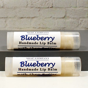 May include: Two tubes of handmade blueberry lip balm with shea butter. The labels are white with blue text that reads "Blueberry Handmade Lip Balm with Shea Butter". The lip balm is in a clear tube.