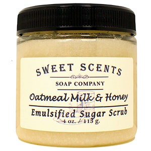 May include: A glass jar with a black lid filled with a light brown sugar scrub. The label reads "SWEET SCENTS SOAP COMPANY Oatmeal Milk & Honey Emulsified Sugar Scrub 4 oz./113 g."