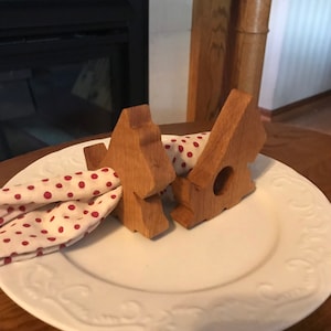 Op de afbeelding: Twee houten kerstboom servetringen die een rood-wit gestippeld servet op een wit bord houden.