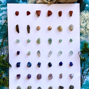 a jumbo styled card of 30 pairs of stainless steel crystal stud earrings. this is sitting on top of ocean paper that is meant to replicate water. the crystal card seamlessly appears to float on the surface.