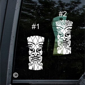 Puede incluir: Dos calcomanías de vinilo blanco de dioses tiki con un diseño estampado. La calcomanía de la izquierda está etiquetada como #1 y la calcomanía de la derecha está etiquetada como #2. La calcomanía de la derecha tiene una guirnalda de flores en la cabeza.