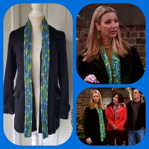May include: A long, knitted scarf in shades of blue, green, and white is displayed on a mannequin wearing a black coat. The scarf is a rectangular shape with vertical stripes. The image also includes a collage of images from the TV show Friends.