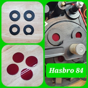 May include: A set of four black circular rings and four matching red circular lenses. The components are shown separately and installed on a black mechanical device with a central metallic coil. The text Hasbro 84 is visible in green.