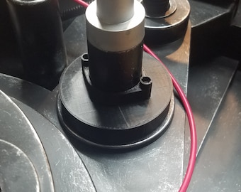 May include: Close-up of a prop from the movie Ghostbusters. The image shows a silver and black component with a red wire, and other black and yellow components. The prop is set against a metallic background.