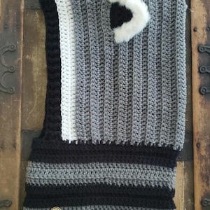 Puede incluir: Un cuello de ganchillo hecho a mano en tonos grises, negros y blancos. El cuello presenta un patr&oacute;n de rayas en la parte inferior y un bot&oacute;n decorativo. Un acento de piel sint&eacute;tica blanca est&aacute; cosido en la parte superior. El cuello est&aacute; dise&ntilde;ado para usarse alrededor del cuello.