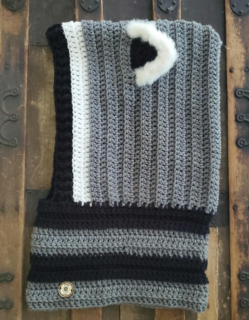 Puede incluir: Un cuello de ganchillo hecho a mano en tonos grises, negros y blancos. El cuello presenta un patr&oacute;n de rayas en la parte inferior y un bot&oacute;n decorativo. Un acento de piel sint&eacute;tica blanca est&aacute; cosido en la parte superior. El cuello est&aacute; dise&ntilde;ado para usarse alrededor del cuello.