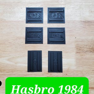 May include: Six black plastic components with a textured surface. Four of the pieces are square with two horizontal raised bars and the letters CB embossed in the center. Two pieces are rectangular with two vertical raised bars and the letters CB.