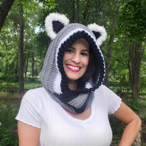 Puede incluir: Una capucha de ganchillo hecha a mano en gris, negro y blanco, con orejas de mapache. La capucha est&aacute; dise&ntilde;ada para usarse alrededor de la cabeza y el cuello. La capucha est&aacute; hecha de hilo suave y es adecuada para el clima fr&iacute;o.