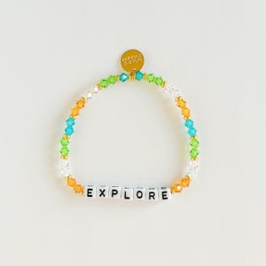 May include: A colorful beaded bracelet with the word "EXPLORE" spelled out in white letter beads. The bracelet features a mix of orange, green, blue, and clear beads. A gold charm with the words "WILD'S CHARM" is attached.