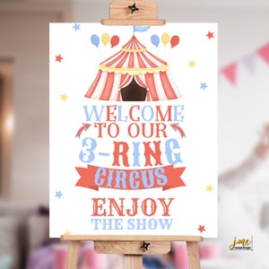 May include: A white sign with a red and white striped circus tent, blue and yellow balloons, and stars. The sign says "Welcome to our 3-Ring Circus Enjoy the Show".