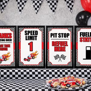 May include: Four framed signs with a racing theme. The signs read "Thanks for Racing Over! Please Take a Favor", "Speed Limit 1", "Pit Stop Refuel Here", and "Fueling Station". Decorations include checkered flags, balloons, and race car cookies.