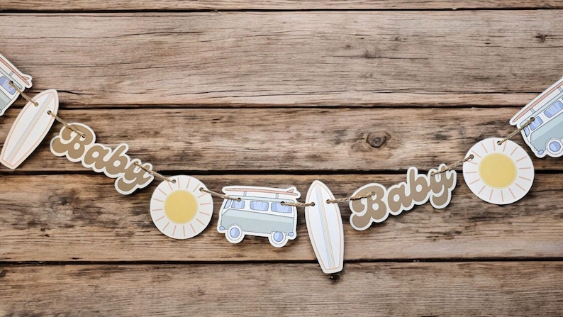 May include: A brown and white baby shower banner with the words "Baby" on it. The banner also features a surfboard, a sun, and a vintage van.
