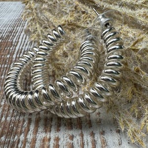 May include: A pair of silver hoop earrings with a coiled design. The earrings are made of a shiny metal and have a simple, modern look.
