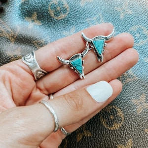 Op de afbeelding: Een paar zilveren oorbellen met turquoise stieren schedel ontwerpen.