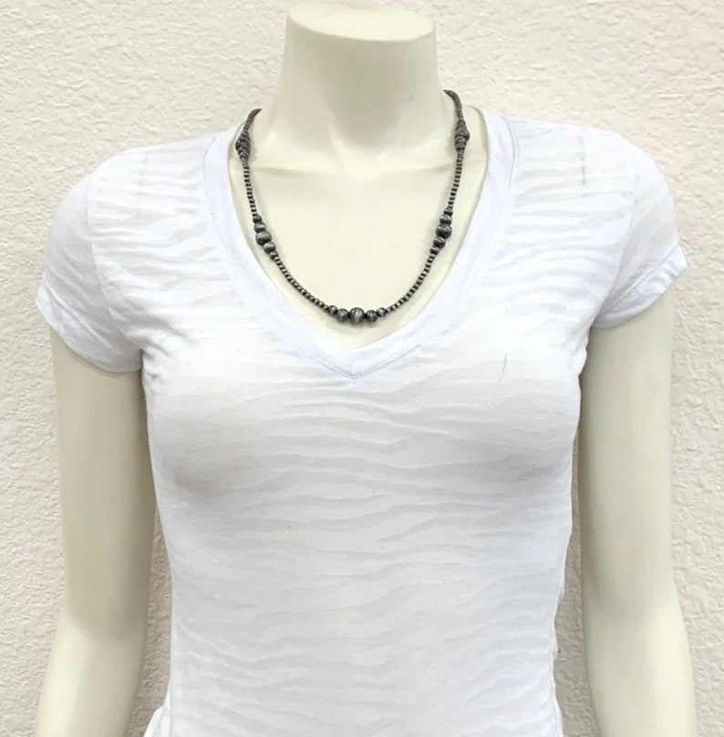 K&ouml;nnte beinhalten: Eine silberne Halskette mit runden Perlen. Die Halskette befindet sich an einem wei&szlig;en Mannequin.