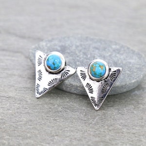 May include: A pair of silver triangle earrings with turquoise stones in the center. The earrings have a decorative design around the stones.