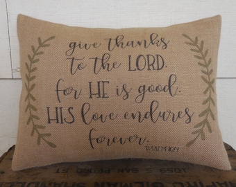 May include: A burlap pillow with a green leafy design and the text "give thanks to the LORD. for HE is good. HIS love endures forever. PSALM 107:1"