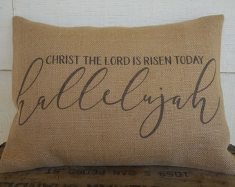 May include: A burlap pillow with the text "CHRIST THE LORD IS RISEN TODAY hallelujah" printed in brown.