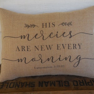 May include: A burlap pillow with the text "His mercies are new every morning" and the scripture reference "Lamentations 3:22-23".