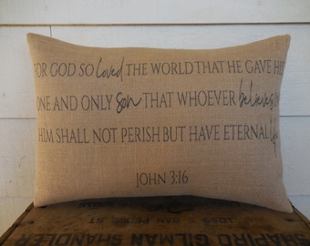 May include: A burlap pillow with the text "FOR GOD SO Loved THE WORLD THAT HE GAVE HIS ONE AND ONLY Son THAT WHOEVER believes IN HIM SHALL NOT PERISH BUT HAVE ETERNAL LIFE" and "JOHN 3:16".