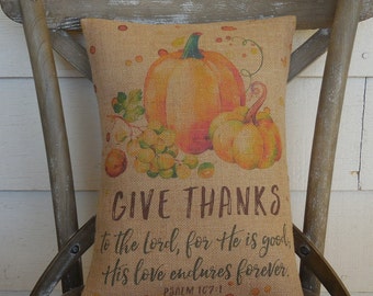 May include: A burlap pillow with a fall-themed design featuring pumpkins, grapes, and the text "GIVE THANKS to the Lord, for He is good, His love endures forever. PSALM 107:1".