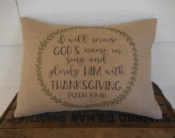 May include: A burlap pillow with a green wreath design and the text "I will praise GOD'S name in song and glorify HIM with THANKSGIVING. PSALM 69:30"