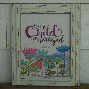 May include: A framed canvas print with the text "For this child I have prayed" and a Bible verse reference, 1 Samuel 1:27. The print features colorful flowers in a whimsical style.