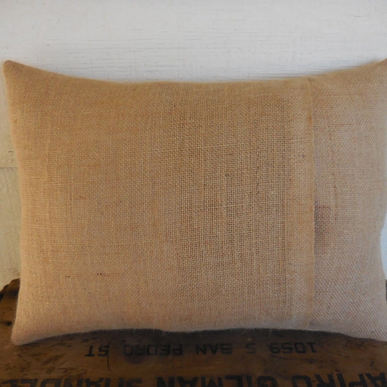 May include: A natural brown burlap pillow cover with a seam down the center back. The pillow cover is made of a woven fabric with a rough texture.