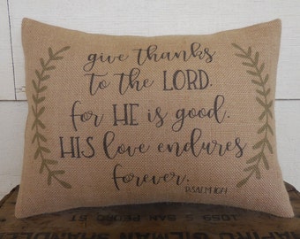 May include: A burlap pillow with a green leafy design and the text "give thanks to the LORD. for HE is good. HIS love endures forever. PSALM 107:1".
