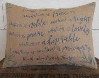 May include: Rectangular burlap pillow with blue text that reads "Finally brothers and sisters, whatever is true, whatever is noble, whatever is pure, whatever is admirable..." with leaf accents. The pillow is on a wooden surface.