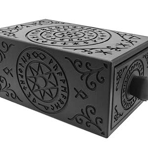 May include: A black rectangular box with intricate, embossed designs. The box features circular and linear patterns with symbols and a central star design. A round knob is on the front. The box has a mysterious, ancient aesthetic.