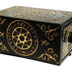 May include: Black wooden box with gold-colored etched designs. The box features circular patterns, starbursts, and ornate scrollwork. A dark wooden knob is on the side. The box has a mysterious, antique aesthetic.
