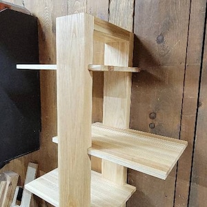 May include: A light wood wall shelf with four shelves. The shelf is mounted to a wood wall.