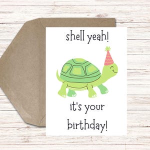 Könnte beinhalten: Geburtstagskarte mit einer Cartoon-Schildkröte mit Partyhut. Die Karte trägt den Text "shell yeah!" und "it's your birthday!". Ein brauner Umschlag befindet sich hinter der Karte.