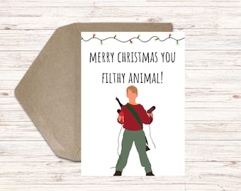 May include: A Christmas card with the text "MERRY CHRISTMAS YOU FILTHY ANIMAL!" and an illustration of a person holding two items. The card is white with a brown envelope.