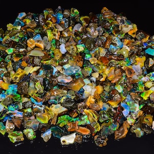 Pode incluir: Um grande monte de bruto de opala colorido, com uma variedade de formas e tamanhos. As opalas são iridescentes e têm um arco-íris de cores, incluindo verde, azul, vermelho e amarelo.