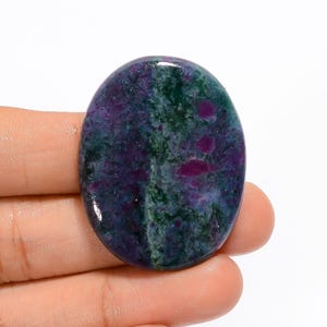 May include: An oval-shaped gemstone with a mix of colors. The stone features a deep purple base with patches of green and spots of bright pink. The polished surface reflects light, highlighting the natural patterns and textures within the stone.