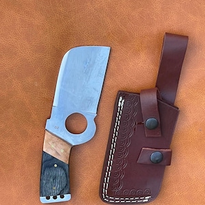 May include: A brown leather sheath with a white stitching design and a black button. A knife with a D2 steel blade and a wooden handle is shown next to the sheath.