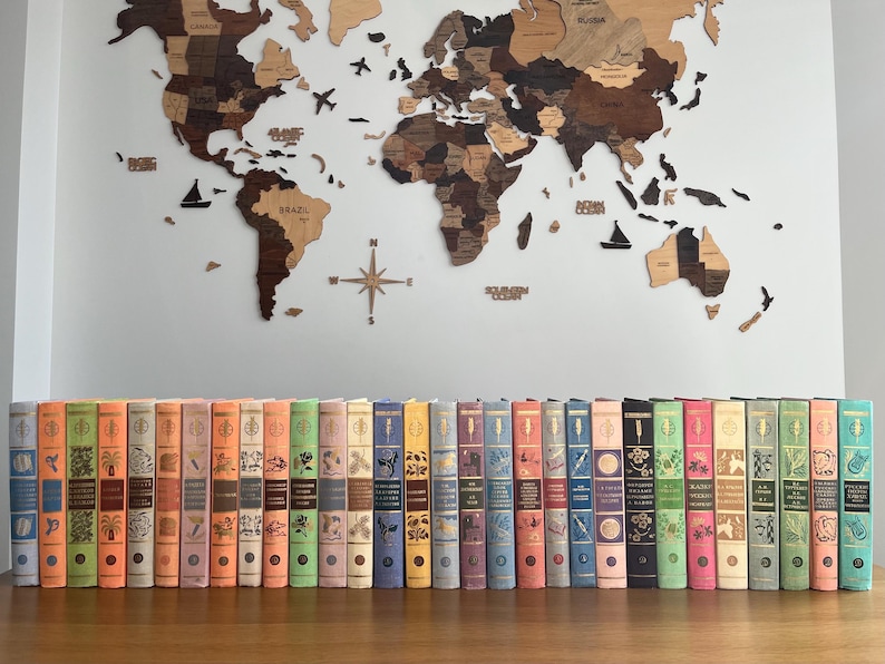 May include: A collection of vintage hardback books with colourful spines and illustrations. The books are arranged in a row on a wooden surface.