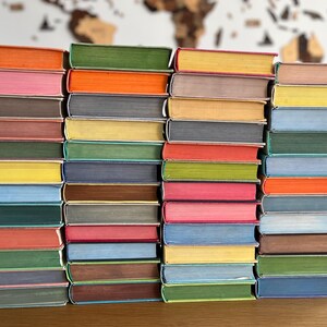 May include: A stack of colourful hardback books with different coloured spines. The books are arranged in a row on a wooden surface.