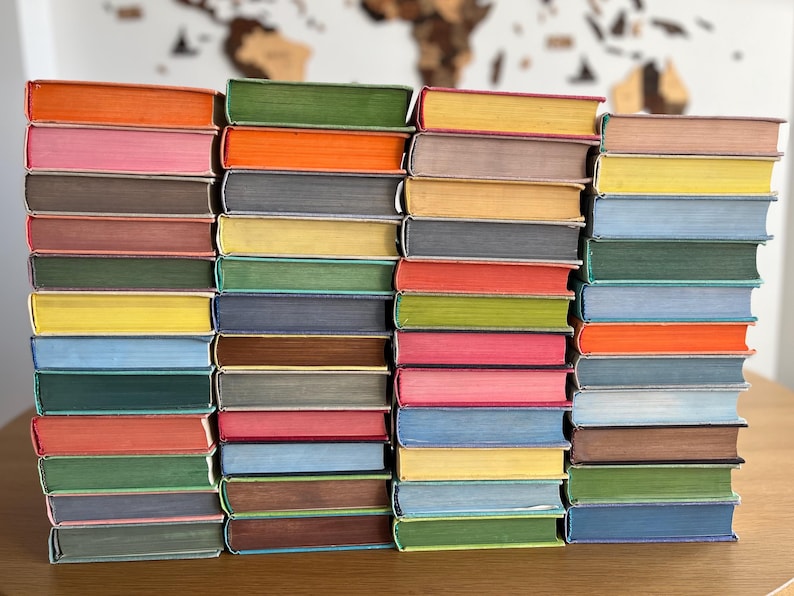 May include: A stack of colourful hardback books with different coloured spines. The books are arranged in a row on a wooden surface.