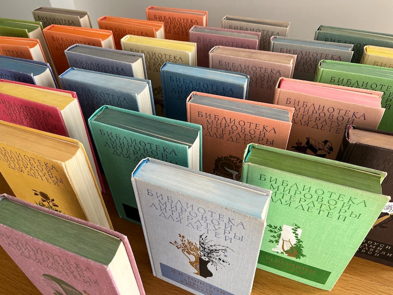 May include: A shelf full of colourful books with the title "Bibliotekа Mirovoy Literatury Dlya Detey" repeated on the spines. The books are arranged in a staggered pattern, creating a visually appealing display.